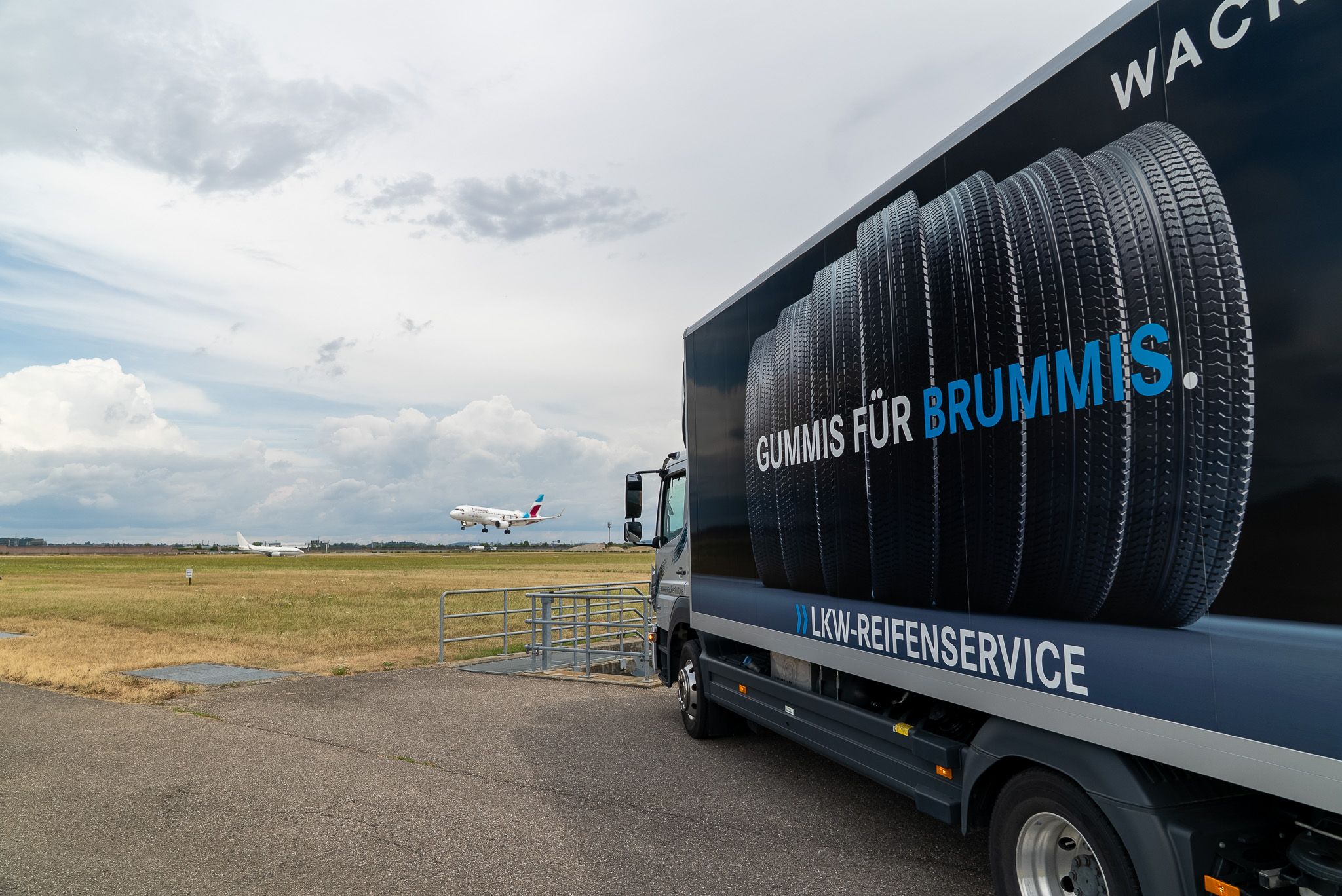 Service- LKW auf Rollfeld, im Hintergrund ein landendes Flugzeug