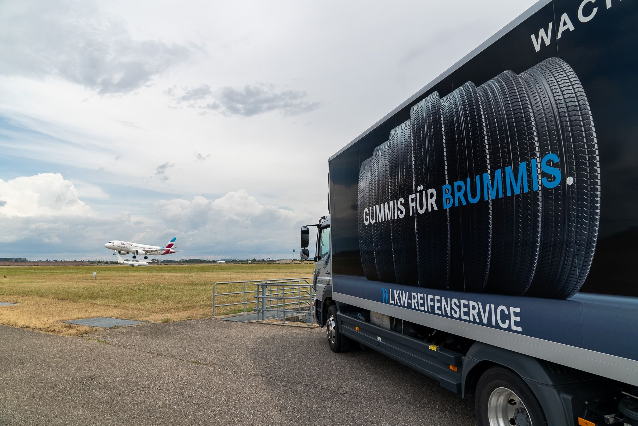 Service-LKW auf dem Rollfeld, im Hintergrund ein landendes Flugzeug