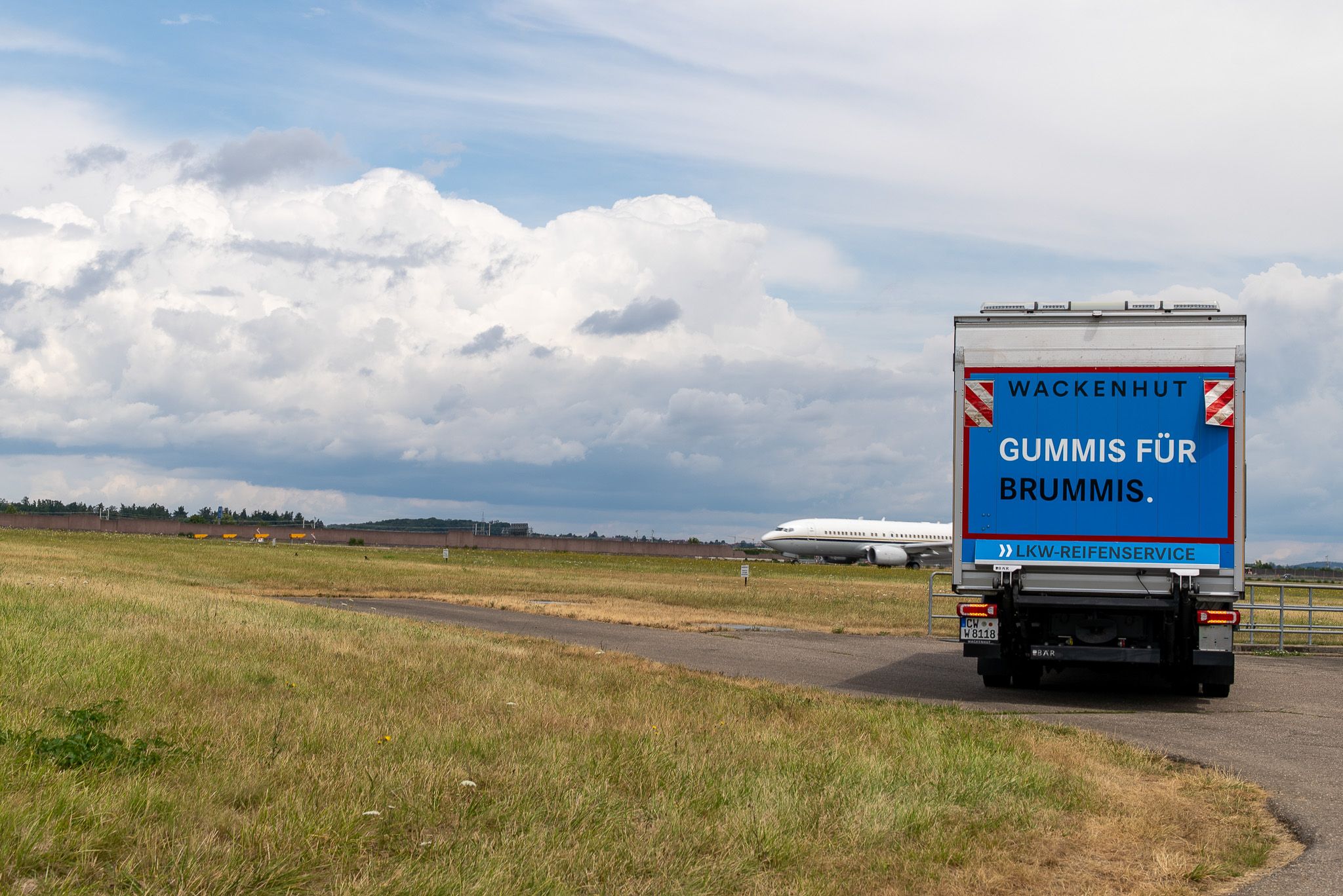 Service-LKW auf dem Rollfeld, im Hintergrund ein landendes Flugzeug