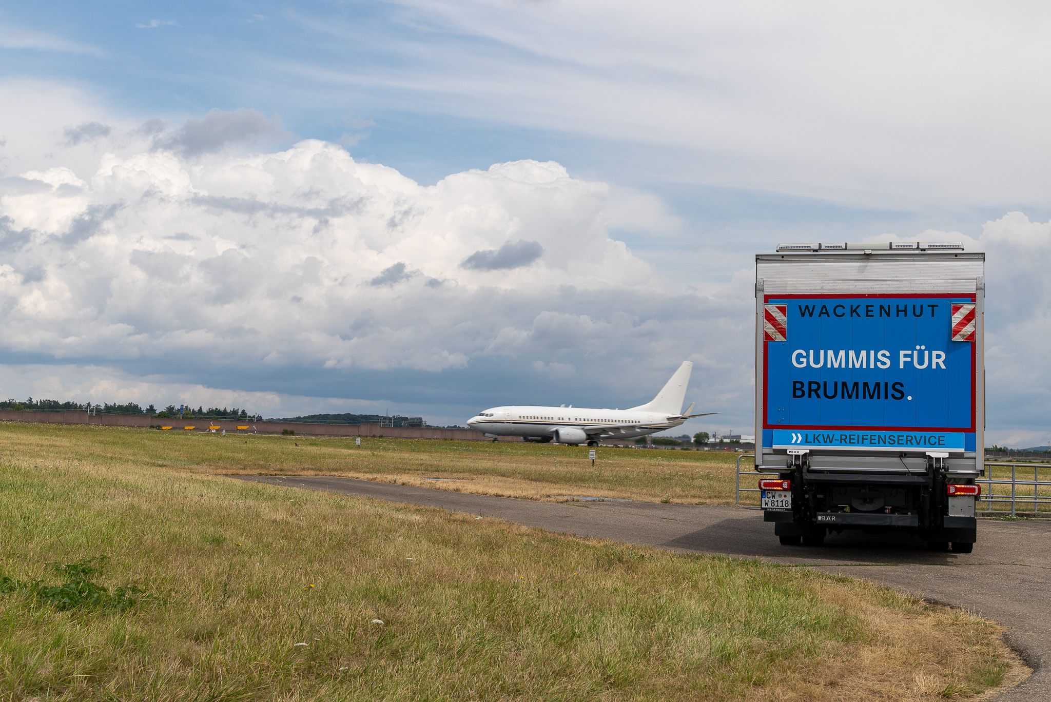 Service-LKW auf dem Rollfeld, im Hintergrund ein startendes Flugzeug
