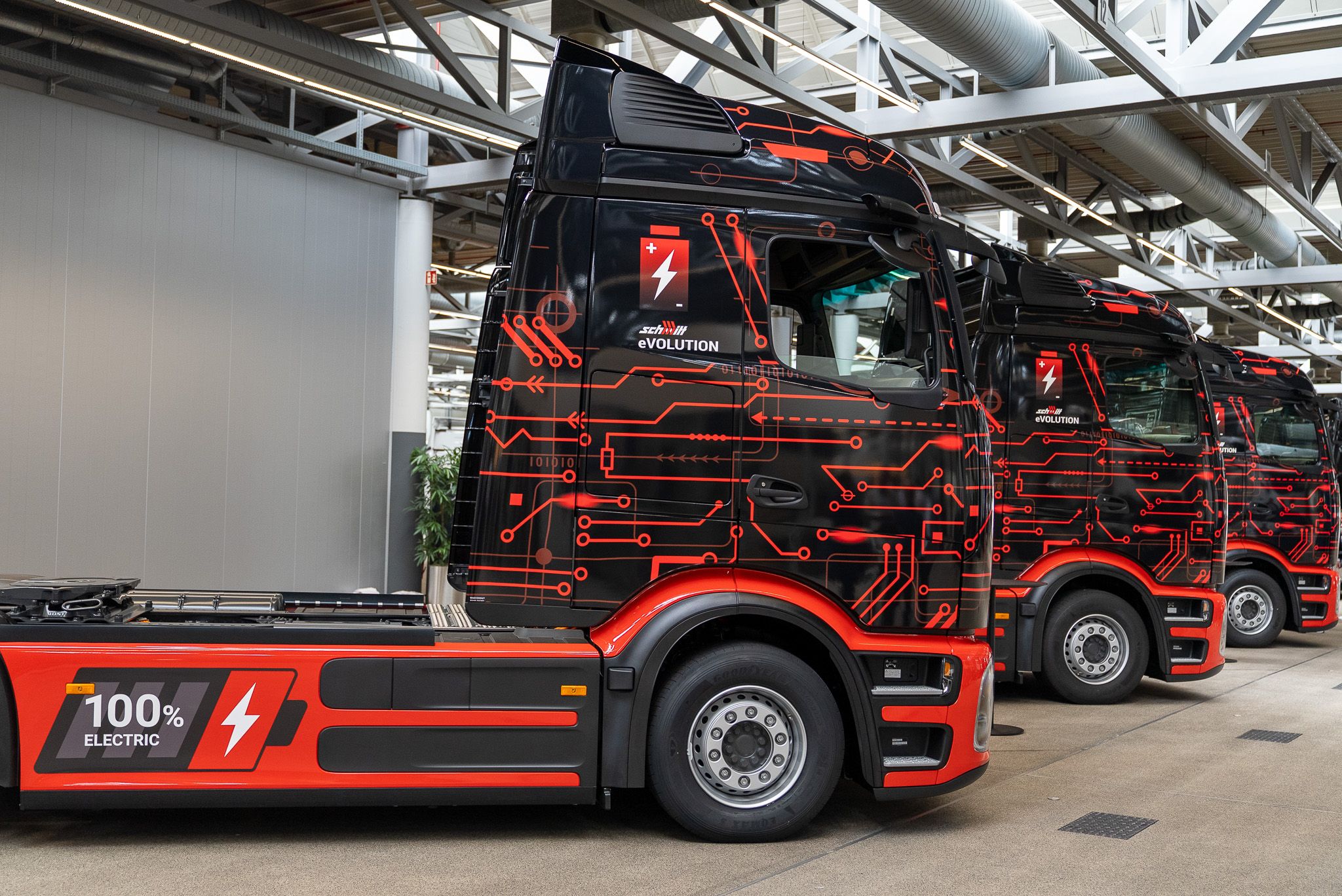 Die E-Actros LKW mit der markanten Logistik Schmitt Folierung stehen in der Auslieferungshalle.