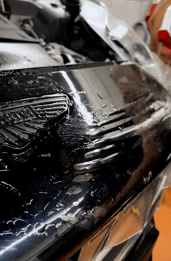 Ein dunkelblaues Aston Martin DB12 Cabrio, an dem gerade eine Lackschutzfolie angebracht wird